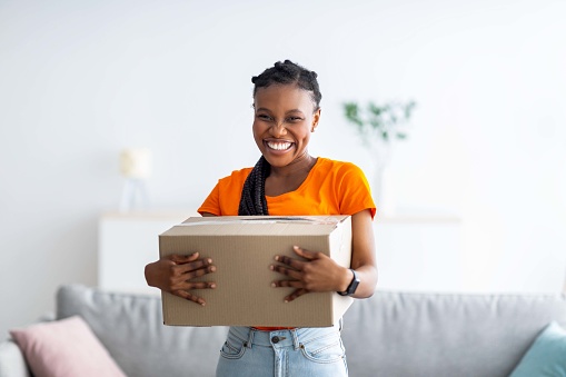 Dama negra encantada sosteniendo un paquete de cartón, recibiendo la entrega deseada, recibiendo su pedido en línea en casa photo