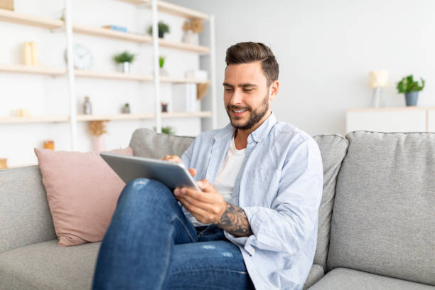 istock Relaxed millennial man resting on sofa with digital tablet, browsing social networks or shopping online, free space 1342064786