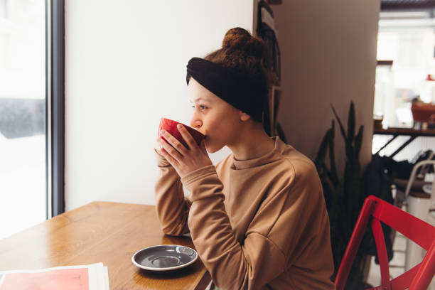 jeune femme ayant une matinée confortable au café - coffee shop coffee break coffee cup holding photos et images de collection