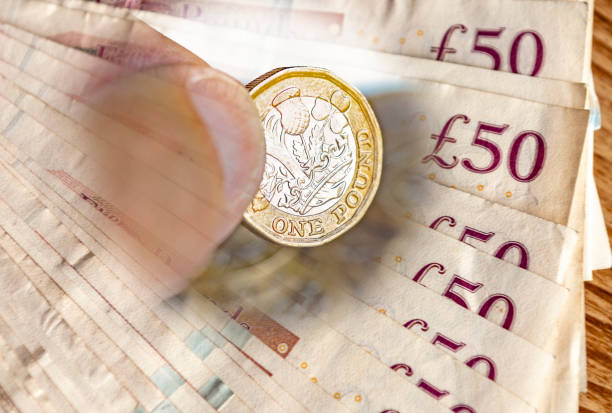Man's hand holding one pound coin Man's hand holding one pound coins blended through fifty pound notes. gold and silver for ira stock pictures, royalty-free photos & images
