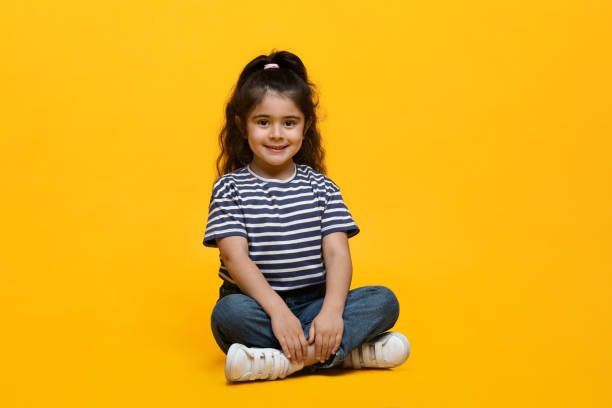 Portrait Of Adorable Little Middle Eastern Girl Posing Over Yellow Background Portrait Of Adorable Little Middle Eastern Girl Posing Over Yellow Background, Cute Small Arab Female Child In Casual Clothes Sitting With Legs Crossed And Smiling At Camera, Copy Space arabic girl stock pictures, royalty-free photos & images