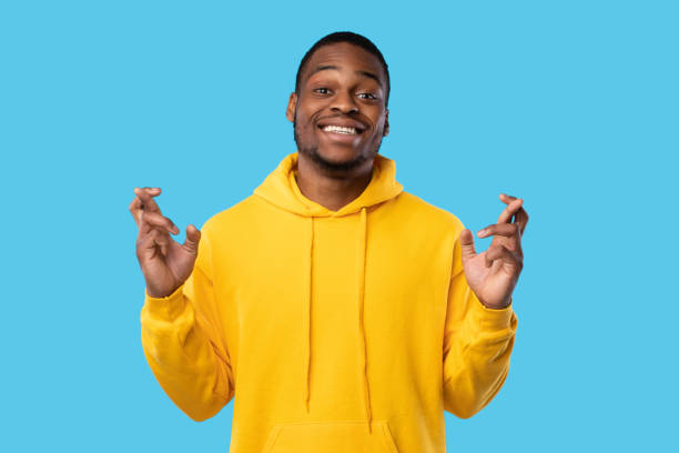 istock African Guy Keeping Fingers Crossed Smiling To Camera, Blue Background 1342065918
