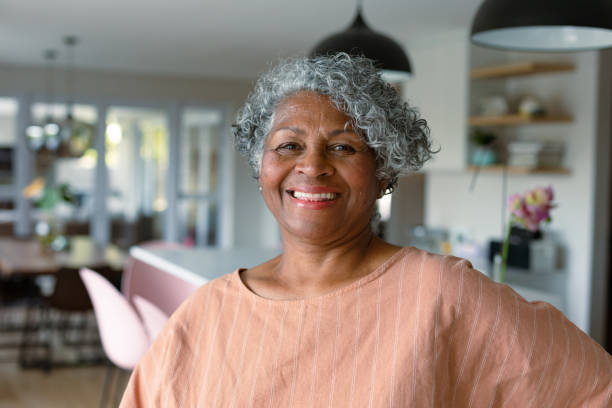 heureuse femme afro-américaine âgée debout dans la cuisine et regardant la caméra - afro photos et images de collection