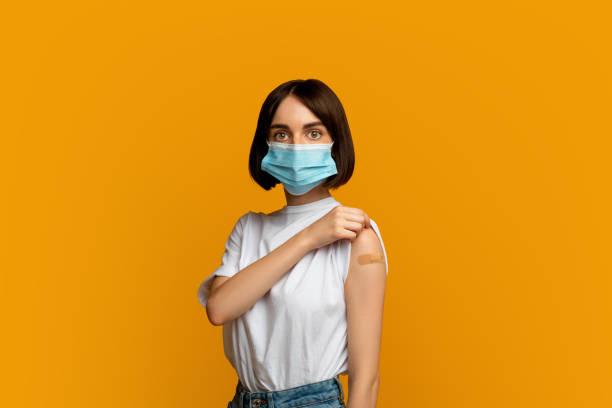 istock Vaccination and immunization concept. Lady wearing protective mask and showing plaster on shoulder after injection 1342067189