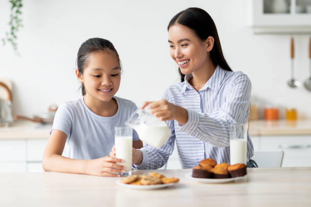 istock Happy asian mom and daughter eating snacks and drinking milk in kitchen interior, having a bite together 1342067516