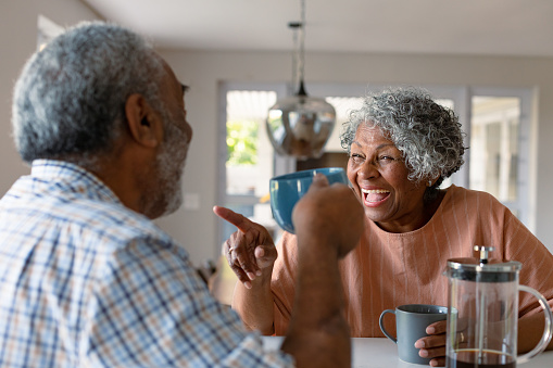 Happy african american senior couple sitting in kitchen with coffee and talking. healthy retirement lifestyle at home.