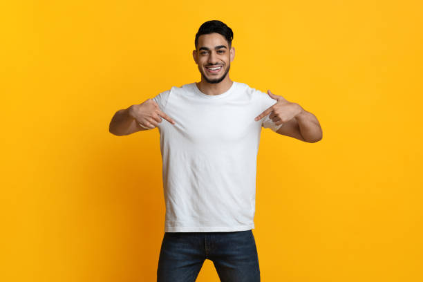 istock Cheerful arab guy pointing at his blank white t-shirt 1342070009