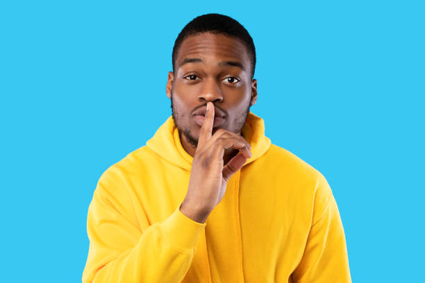 istock Black man gesturing finger-on-lips sign looking at camera, blue background 1342070146