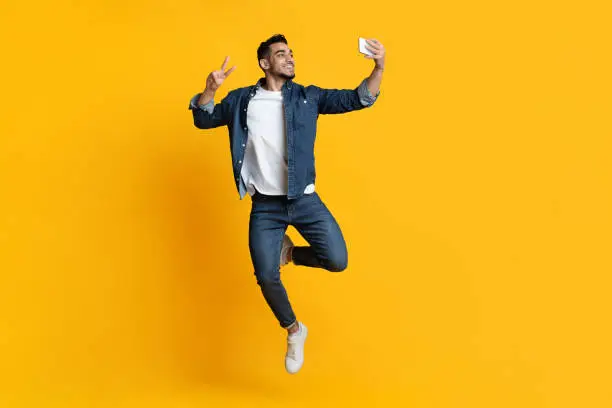 Photo of Cheerful handsome arab man taking selfie on yellow