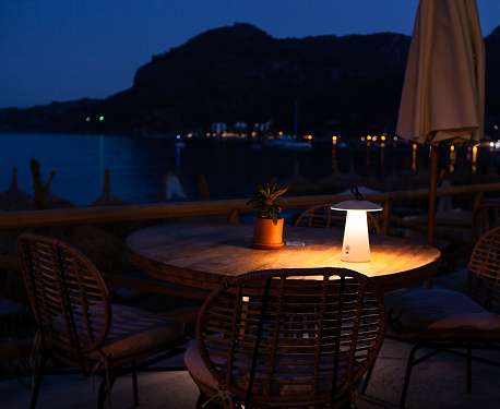 Dining table on the embankment at night, romantic dining in luxury resort. Cafe on beach with seaview. Romantic soft warm light lamp on table. outdoor cafe