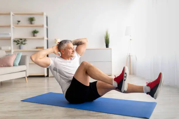 Photo of Sports during lockdown. Mature man doing home fitness on yoga mat, working out whole body at home