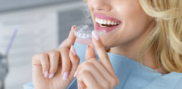 Unrecognizable female patient holding invisible braces or trainer, panorama Banner for invisalign orthodontics, modern dentistry concept. Unrecognizable blonde woman with healthy white teeth holding invisible braces while sitting at dental chair, closeup portrait, copy space dentist photos stock pictures, royalty-free photos & images