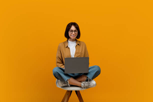 concepto de e-learning. estudiante que usa una computadora portátil mientras está sentada en la silla sobre fondo amarillo, espacio de copia - red chairs fotografías e imágenes de stock