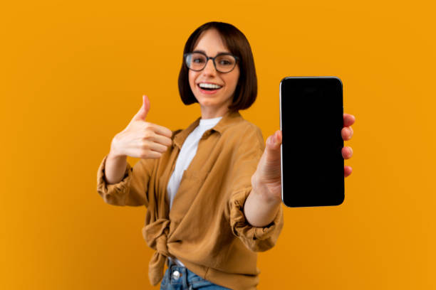 istock I recommend this app. Excited lady holding smartphone with blank screen, showing device and thumb up, yellow background 1342074874
