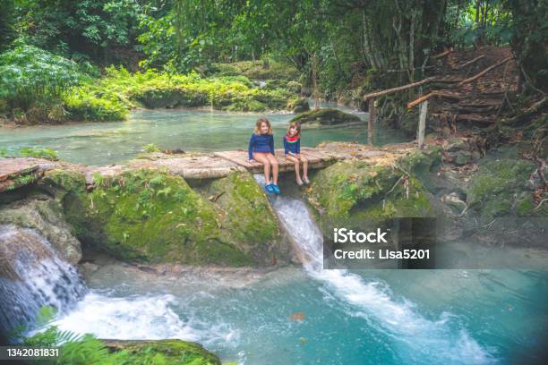 Children Sit By A Lush Tropical Lagoon Waterfall On A Family Vacation Stock Photo - Download Image Now