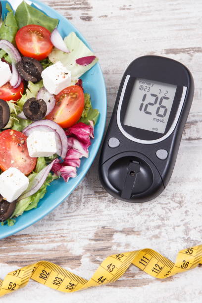 Glucometer with sugar level and greek salad with feta cheese and vegetables. Best food for diabetics, dieting and slimming stock photo
