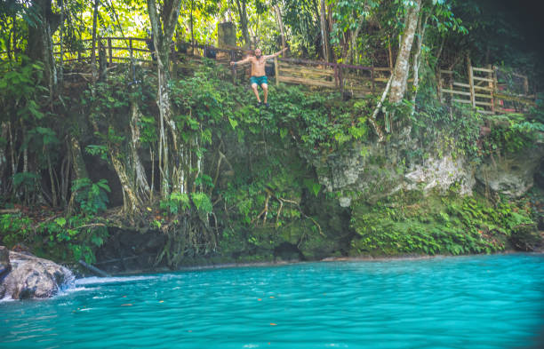 человек прыгает со скалы в лагуну внизу. очо риос ямайка - waterfall tropical rainforest water jamaica стоковые фото и изображения