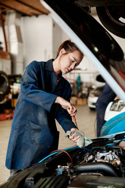 shot of a female mechanic holding a dipstick while checking a car's oil level - automobile industry transportation indoors vertical imagens e fotografias de stock