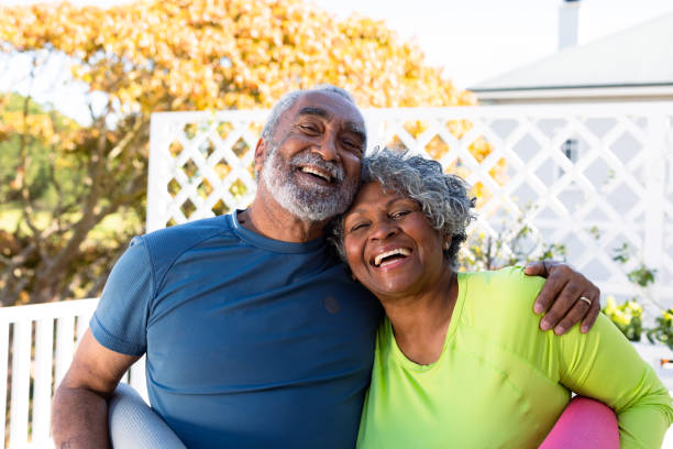 coppia di anziani afroamericani sorridente che tiene tappetini da yoga in giardino e guarda la macchina fotografica - gardening couple senior adult ethnic foto e immagini stock