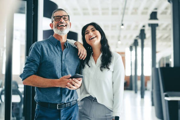 zwei glückliche kollegen lächeln, während sie zusammen stehen - business businessman cheerful happiness stock-fotos und bilder