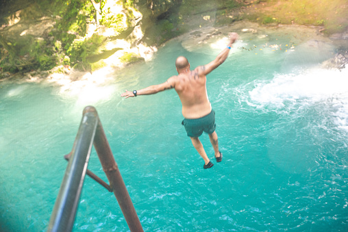 Man dives from a cliff into the turquoise blue water below