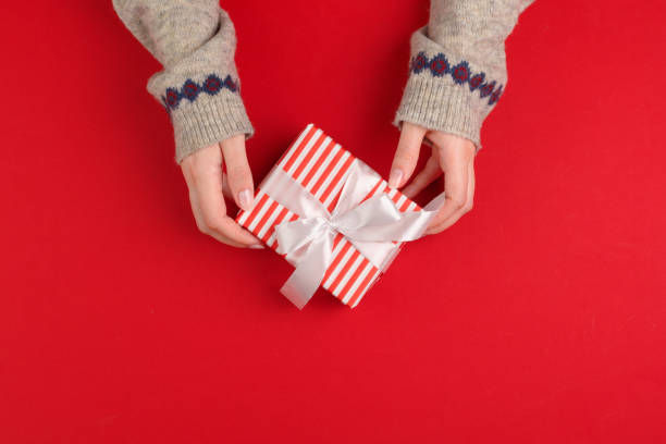 istock Female hands with christmas gift on red background, top view, copy space 1342086866