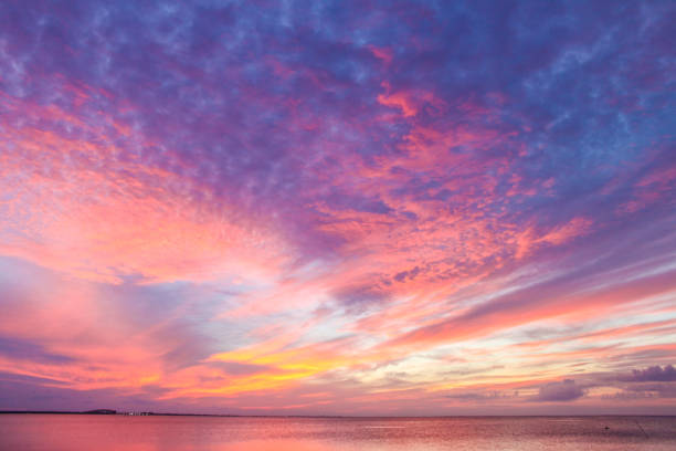 Glorious beautiful colorful sunset with colors stringing out from horizon over ocean with yellow and pink bursting into dappled purple near the top