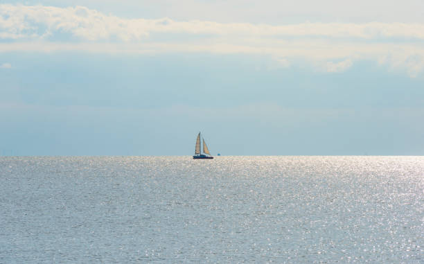 istock Sailboat sailing in bright silver colored sunlight reflected by the water surface of a lake under  a blue white sky in summer 1342089115