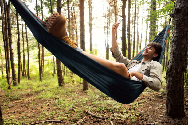 randonneur masculin souriant se reposant dans un hamac dans la forêt de pins et prenant un selfie - hamac telephone homme photos et images de collection