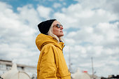 An urban young woman in yellow jacket against blue sky 1