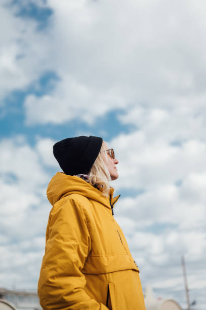 una joven urbana con chaqueta amarilla contra el cielo azul 1 - people personal accessory town hat fotografías e imágenes de stock