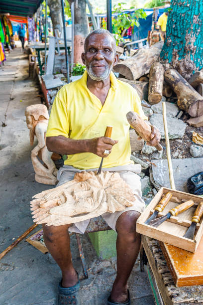 jamaican man uses hand tools to carve a decorative art sculpture from raw wood - jamaican culture imagens e fotografias de stock