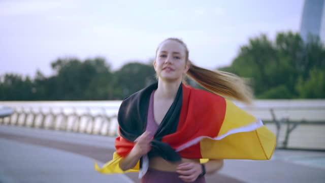 Cheerful young woman running wrapped in Germany flag, representing her country