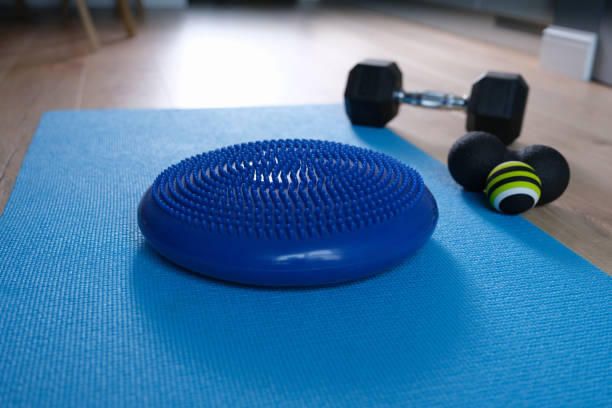 coussin d’équilibre bleu allongé sur un tapis près des haltères et rouleau de balle à la maison en gros plan - massage ball photos et images de collection