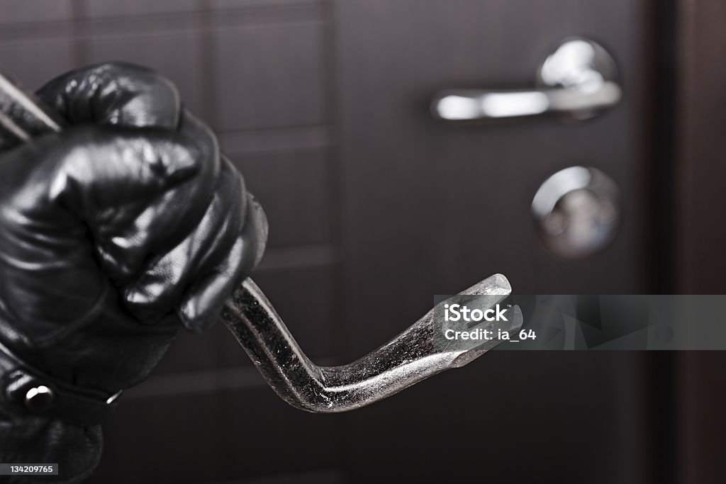 Burglar hand holding crowbar break opening door Crime scene - thief or burglar hand in gloves holding metal crowbar break opening home door lock Burglary Stock Photo