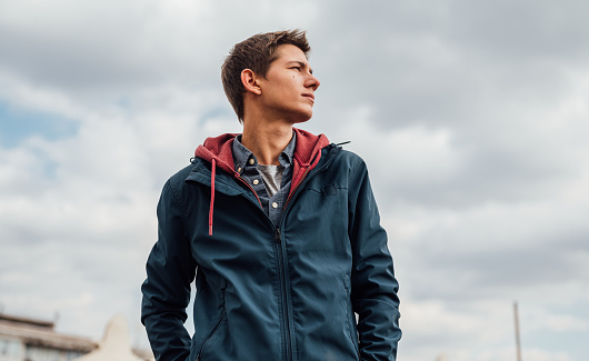 A low angle view of a young urban man in a blue jacket looking away