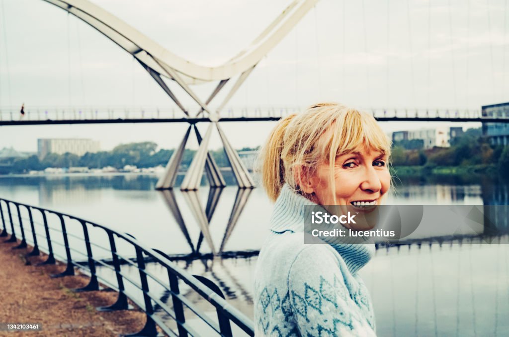 The Arc of Living Happy mature woman leaning on the quayside rail early morning near the Infinity Bridge at Stockton on Tees, England. People Stock Photo