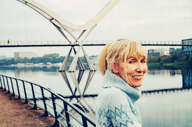 The Arc of Living Happy mature woman leaning on the quayside rail early morning near the Infinity Bridge at Stockton on Tees, England. cleveland england stock pictures, royalty-free photos & images