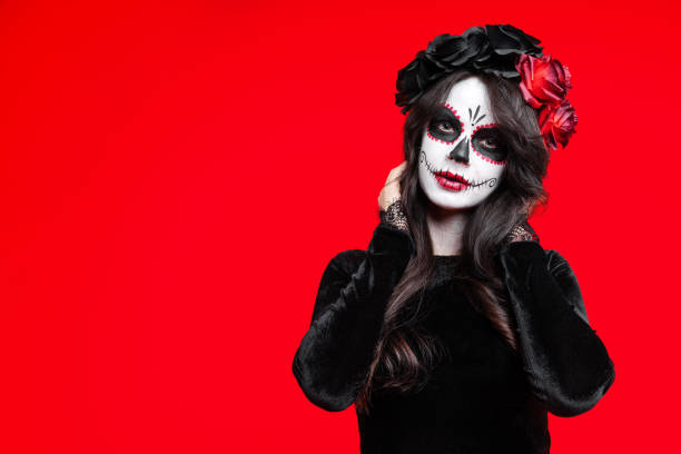 Sugar skull makeup on happy Halloween party Girl with creative sugar skull makeup with a wreath of flowers on head, wide isolated on red background. Holiday concept Dia De Los Muertos on poster for Halloween party or La Calavera Catrina. painted masquerade masks stock pictures, royalty-free photos & images