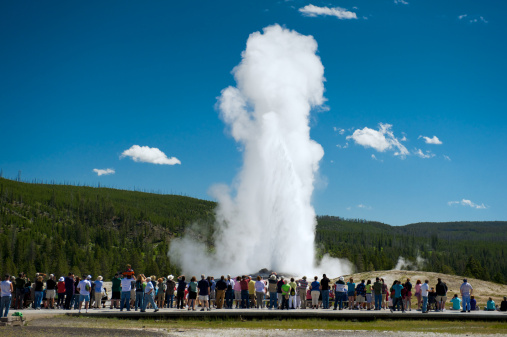 Tourists gather to watch as Old Faithful geyser in Yellowstone National Park erupts forcing out boiling water and steam from the bedrock below.