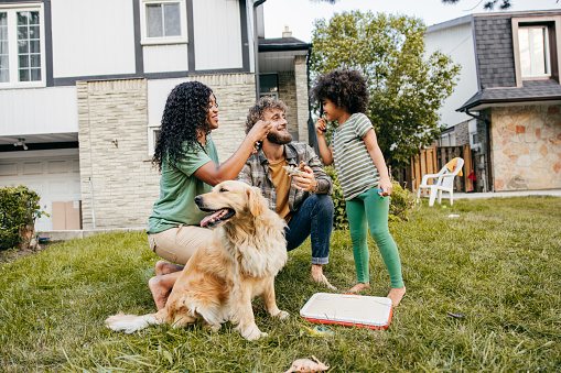 Couple, daughter and their dog all spending time together outside on their lawn.