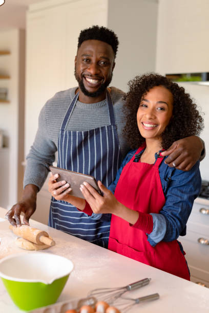 istock Happy african american couple wearing aprons, baking together and using tablet 1342113196