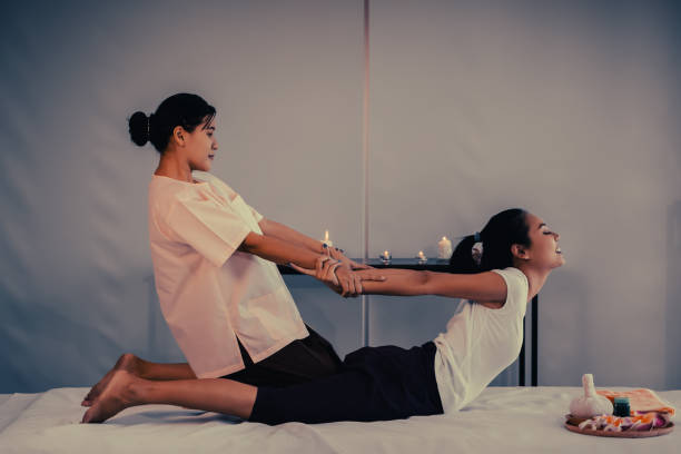 il massaggiatore sta dando alla donna asiatica un back stretching in un trattamento thai massage spa - massaging relaxation indoors traditional culture foto e immagini stock