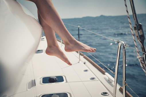 a Closeup shot of young female legs with a yacht in the sea waters in the background