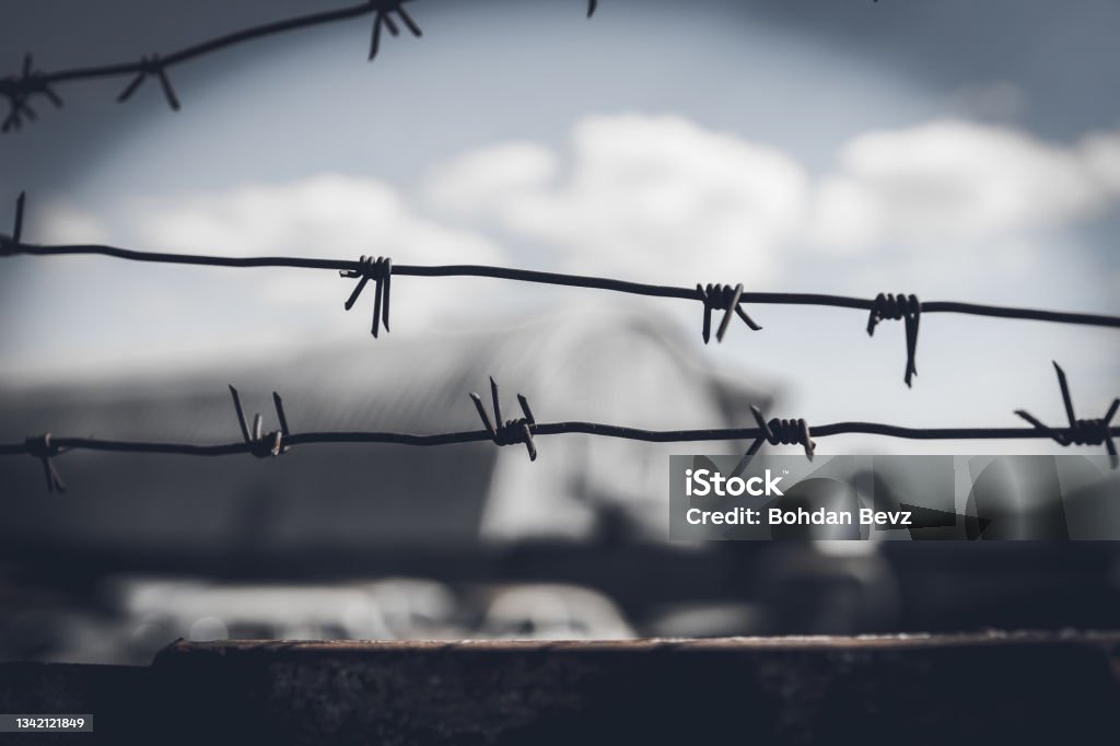 Barbed wire fence against dramatic, dark sky Barbed wire fence against dramatic, dark sky. Holocaust Stock Photo