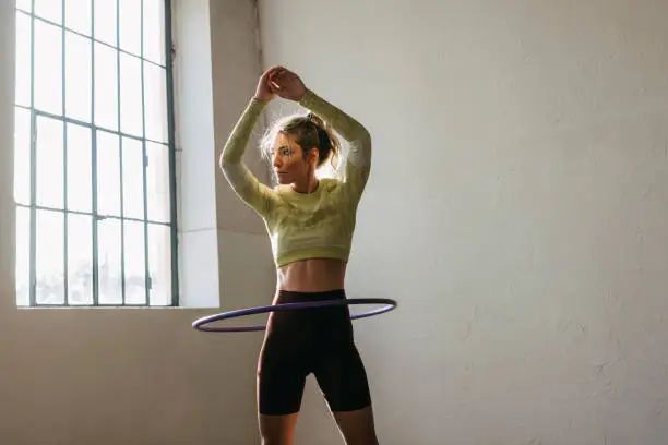 Young female in sportswear exercising with hula hoop in gym