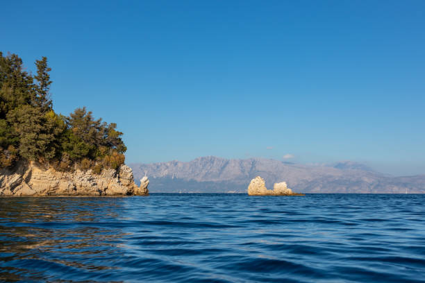 Sunset rocks in vivid blue water of Ionian Sea with rocky green cliffs and clear sky. Nature of Skorpios island near Lefkada in Greece. Summer travel