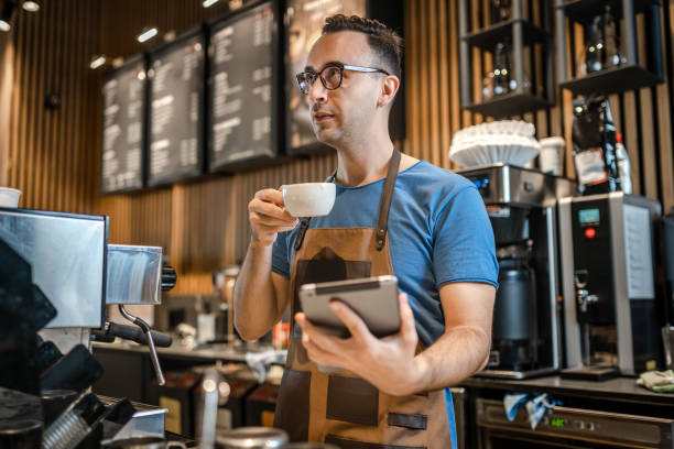 istock Male barista checking orders on digital tablet and drinking coffee 1342125644
