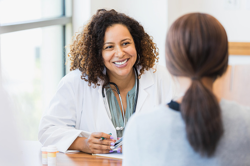 A smiling mid adult female doctor listens as a female patient discusses her health.