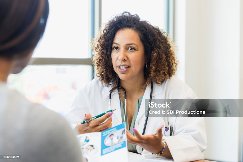 Female doctor discusses healthcare with patient A serious female doctor gestures as she discusses healthcare options with a mature female patient. The patient is reading an informational brochure. Doctor Stock Photo
